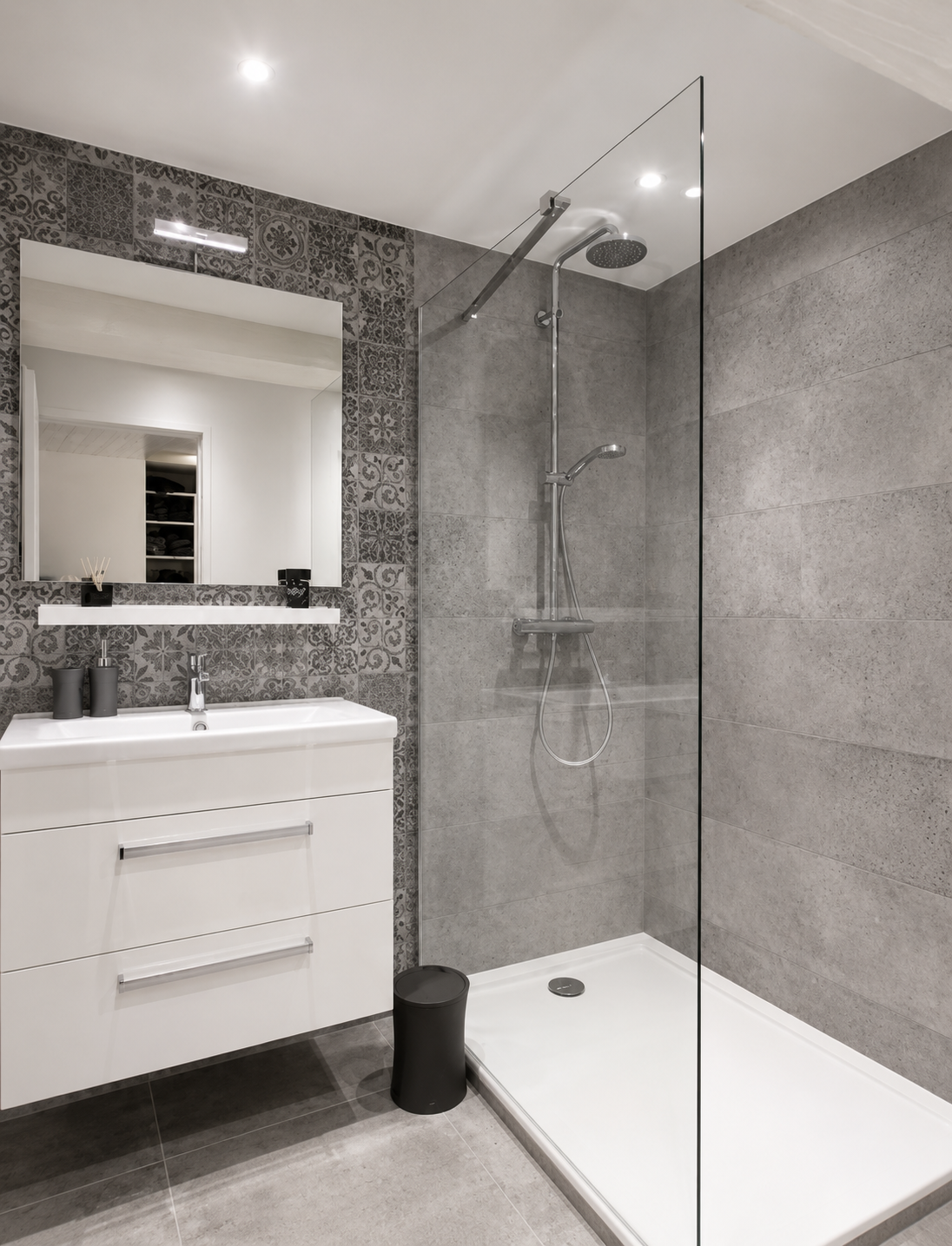 Baño renovado con ducha de cristal, mueble blanco y revestimiento gris