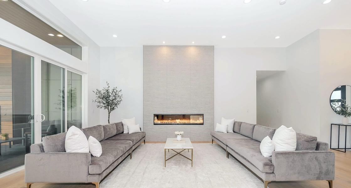 Salón luminoso con chimenea lineal, sofás grises y ventanales